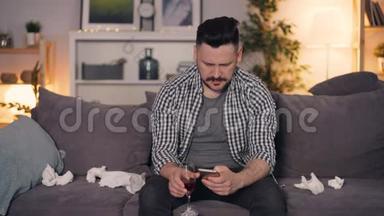 一个情绪低落的家伙，一个人坐在家里，用智能手机端着酒杯喝酒